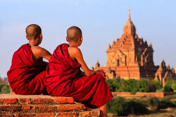 Young Buddhist monks sitting on the temple and looking at the view of ancient Bagan, Myanmar (Burma)