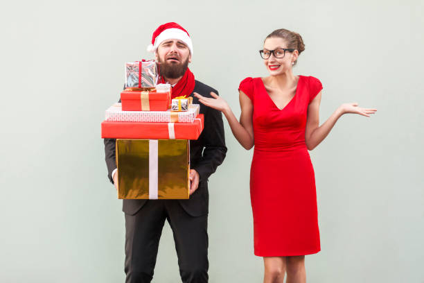 istock Its so hard and i tired! Not my problem, everything fine. Bearded man holding many gift box and crying, women looking at camera, toothy smiling and hands on sides and say so what? 860789888