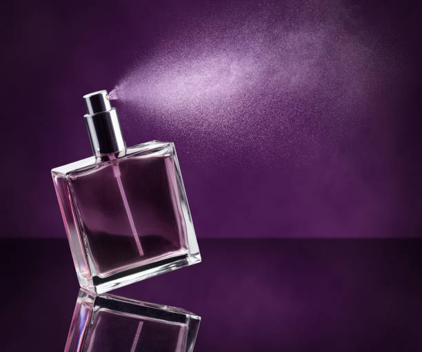 perfume de rociadura sobre fondo púrpura - perfumado fotografías e imágenes de stock