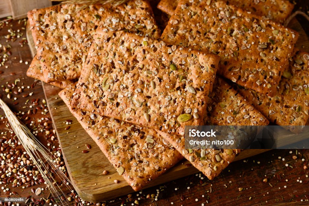 brown crackers topped with seeds high-angle shot of some brown crackers topped with different seeds on a chopping board placed on a rustic wooden table Appetizer Stock Photo