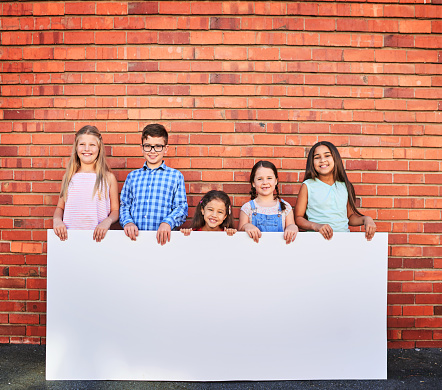 Portrait of a group of young children holding a blank sign against a brick wall