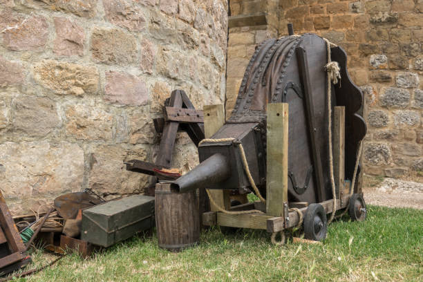 A rustic blacksmith workshop featuring an old white plaster forge surrounded by vintage tools and ironworking equipment. Rusted rings, tongs, hammers, and a hand-cranked grinding wheel evoke the atmosphere of traditional craftsmanship and early metalworking.