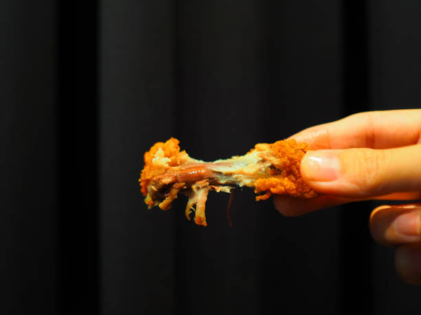 istock Eaten fried chicken wing held by right hand, black curtain background 860812514