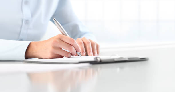 Woman's hands writing on sheet  in a clipboard with a pen, isolated on desk