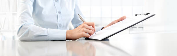 Woman's hands writing on sheet  in a clipboard with a pen, isolated on desk