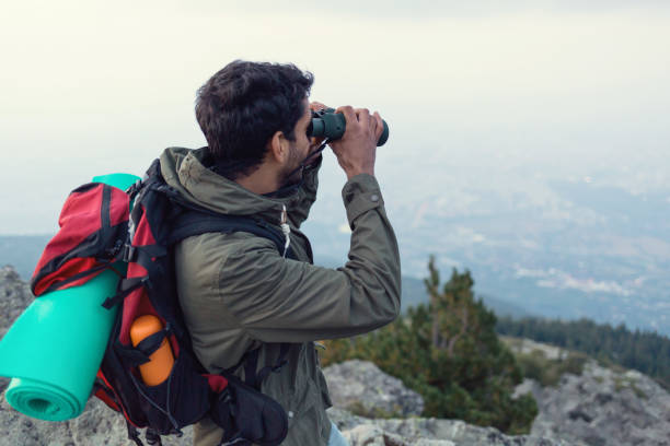 istock Young man standing on the mountain peak and looking through binoculars 860830178