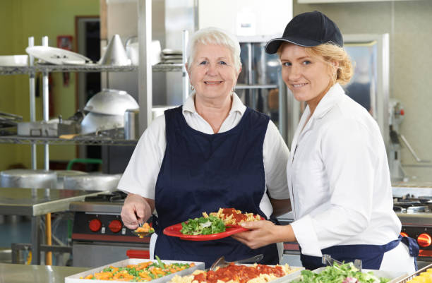 Portrait Of Two Dinner Ladies In School Cafeteria Portrait Of Two Dinner Ladies In School Cafeteria cafeteria worker photos stock pictures, royalty-free photos & images