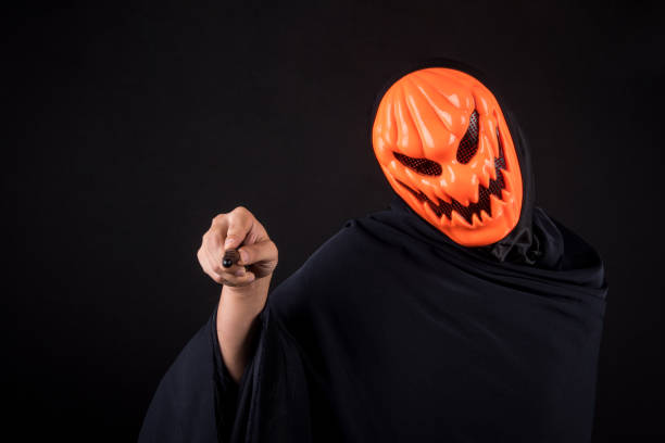 istock Mystery man with orange pumpkin evil mask holding magic wand on black background 860860134
