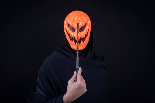 istock Mystery man with orange pumpkin evil mask holding magic wand on black background 860860320
