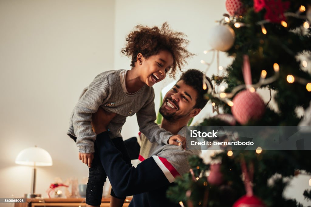 Reaching for the top of the Christmas tree! Shot of an african american father and daughter celebrating Christmas with love at home. Christmas Stock Photo