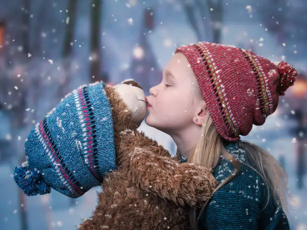 Photo of A little girl kisses a Teddy bear. snowing, winter