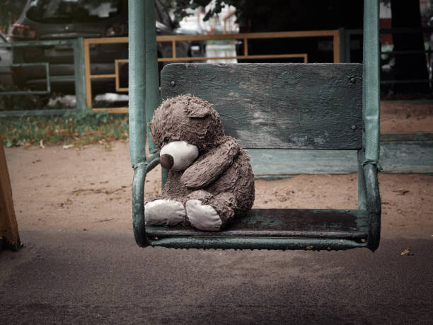 Miserable wet Teddy bear on a swing in the rain