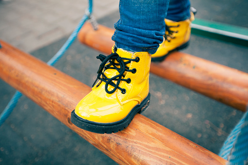 Little boy legs with yellow boots on playground.