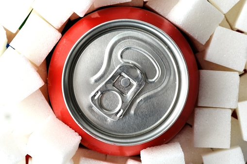 Sugar overdose in soft drinks with red soda can surrounded by white sugar cubes