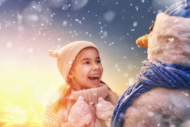 Happy child girl playing with a snowman on snowy winter walk in nature. Frost winter season.
