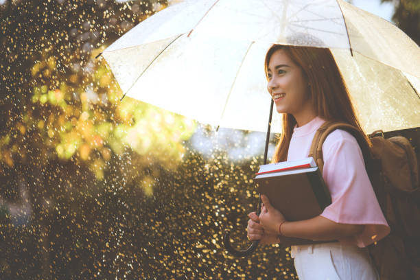 アジアの学生が、雨を待っている彼女は傘を持っていた。 - umbrella women storm yellow ストックフォトと画像