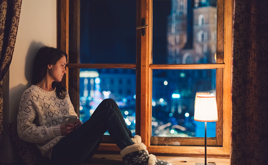 Relaxed woman sitting at the window sill and drinking tea