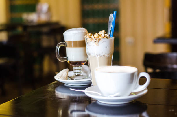 Three different coffee cups and on darck caffee background. Cappuccino, latte and frappe on table. Coffee shop with cups of different coffee with milk