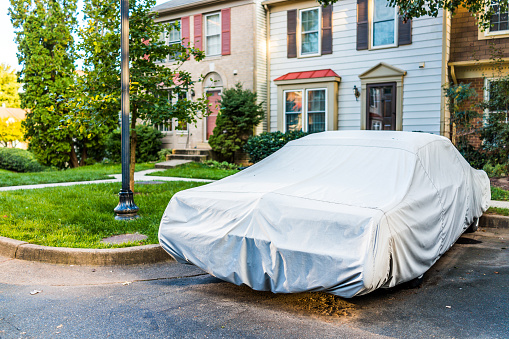 Vintage car covered with protective cover by townhouse for wet weather in parking lot