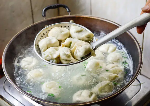 Chinese Family Cooking Boiled Dumplings. The dumplings are picked up from the wok.