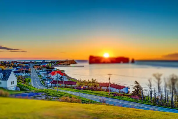 Photo of Famous Rocher Perce rock in Gaspe Peninsula, Quebec, Canada, Gaspesie region with cityscape at sunrise and sun with rays
