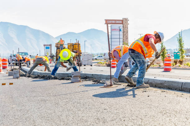 Road construction worker scoups up concrete while cleaning up a center medium just laid in Spanish Fork, Utah. Other workers smooth out the center medium with a float Spanish Fork, UT, USA – August 3, 2017: Road construction worker scoups up concrete while cleaning up a center medium just laid in Spanish Fork, Utah. Other workers smooth out the center medium with a float spanish fork utah stock pictures, royalty-free photos & images