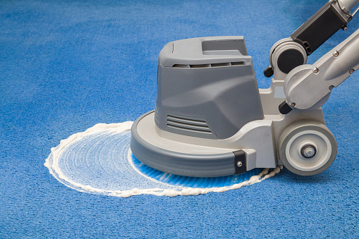Químico de la alfombra azul que hace espuma, frotando y limpieza con máquina de disco profesionalmente. Limpieza regular de comienzos de la primavera. Concepto de servicio de limpieza. photo