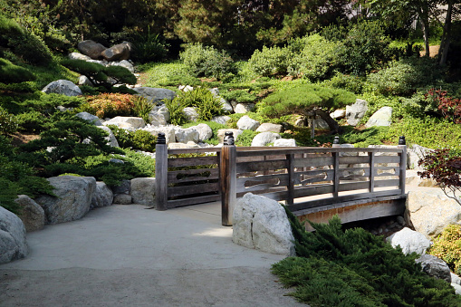 Kamloops, Canada - September 24, 2022: A small orange bridge spans a dry riverbed at the Uji Friendship Garden in Riverside Park, downtown Kamloops. Established on Canada Day, July 1st, 2000, this Japanese garden in a Canadian setting marks an international friendship between the sister cities of Uji, Japan, and Kamloops, Canada.