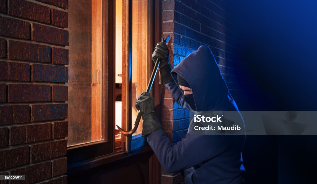 Burglar breaking into a home Hooded masked burglar forcing open a window in a home. Burglar Stock Photo