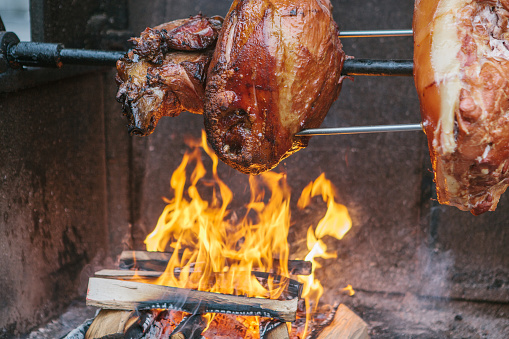 Large chunks of delicious pork hams cooked on an open fire. The street food. Food outdoors. Camping and cooking on a spit over the fire. Camping.