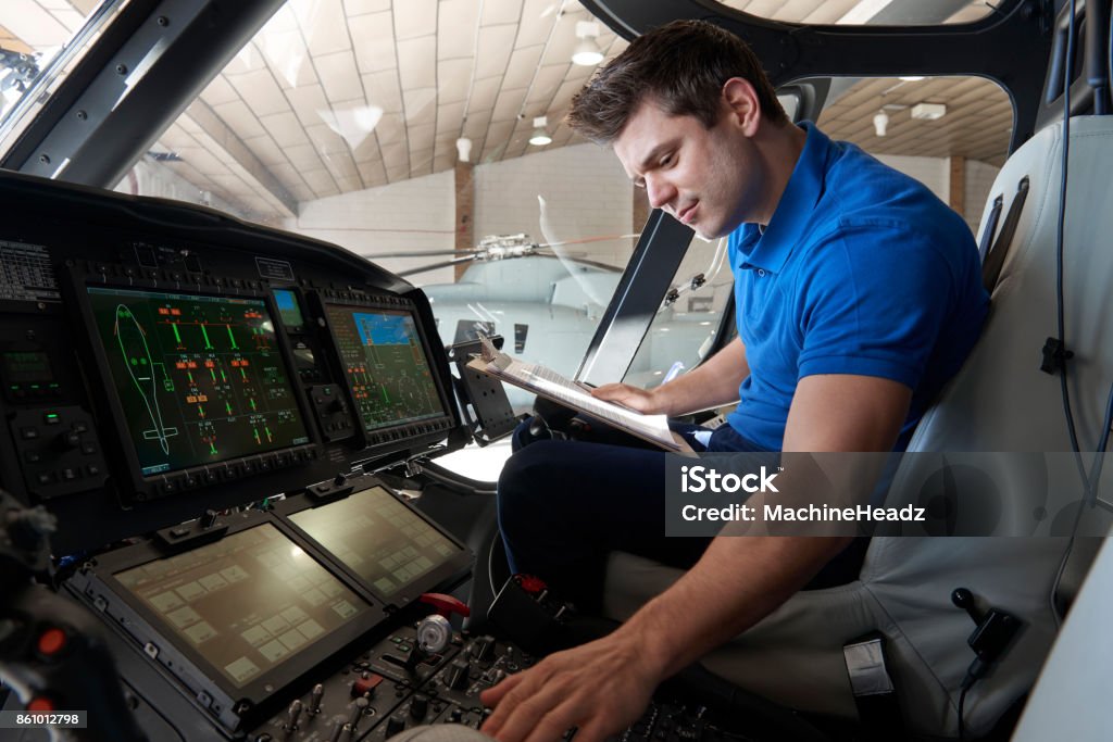 Male Aero Engineer With Clipboard Working In Helicopter Cockpit Repairing Stock Photo