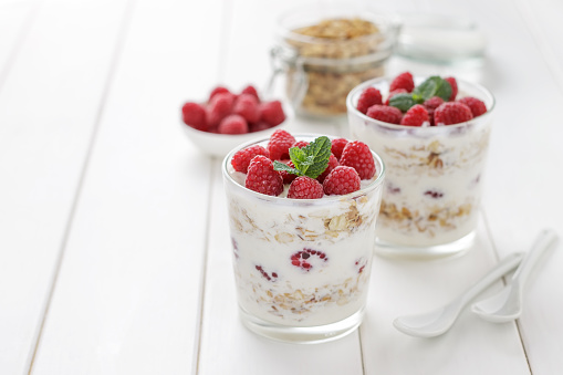 Healthy breakfast yogurt with granola and raspberries in glasses on white wooden table. Morning dessert on light background with copy space.