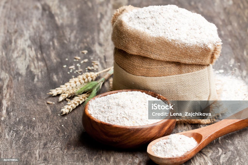 Whole  grain flour in a wooden bowl and sackcloth bagwith ears Flour Stock Photo