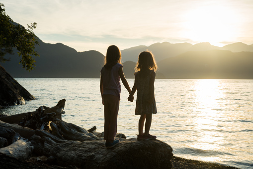 Sisters holding hands at sunset by the sea at Porteau Cove, BC, Canada