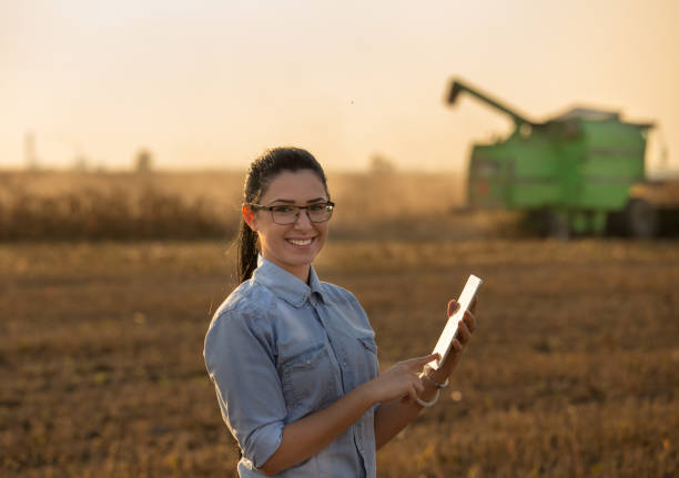 Agronomist with tablet in front of combine harvester Pretty young woman with tablet standing in soybean field with combine harvester working in background agronomist photos stock pictures, royalty-free photos & images