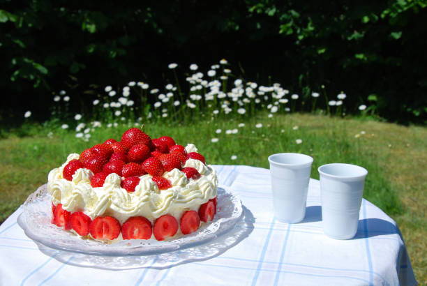 Fresh strawberry cake and two mugs on a table in a garden with blossom daisies