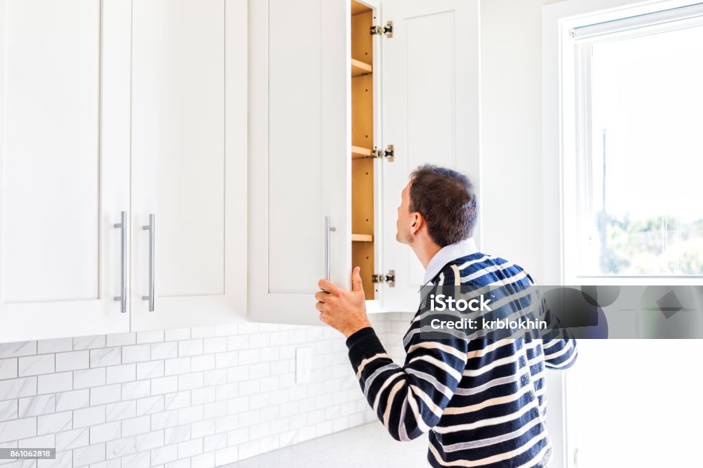 Young man checking looking inside empty kitchen modern cabinets by window after or before moving in Cabinet Stock Photo