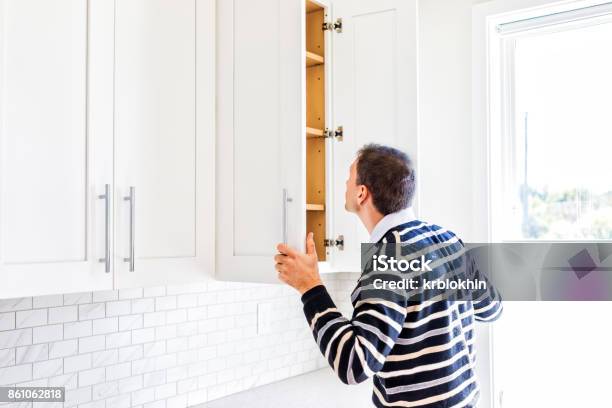 Young Man Checking Looking Inside Empty Kitchen Modern Cabinets By Window After Or Before Moving In Stock Photo - Download Image Now