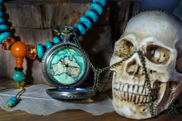 Photo of Still life photography pocket watch , bead necklace and blured human skulls in dark vintage tone