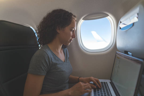 istock Young Eurasian woman working on laptop while seated by a window on an airplane 861064590