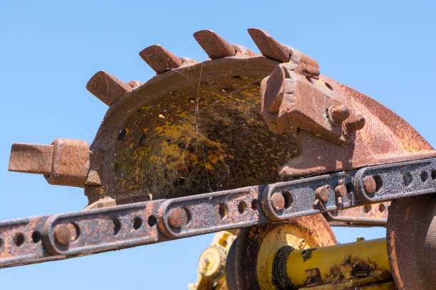 Abstract textures and shapes: Aging metal machinery parts from an old digger including the chain and one of the 6 tooth digger components. Complete with rust, and yellow paint bubbling and corroding with age.