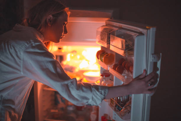 Woman in front of the refrigerator late night Woman in front of the refrigerator late night eating disorder stock pictures, royalty-free photos & images