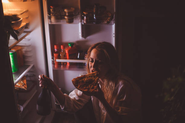 giovane donna che beve e mangia a tarda notte - brutta abitudine foto e immagini stock