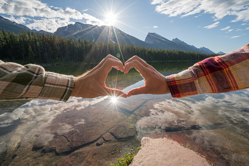 Young couple making a heart shape frame together on mountain lake landscape 
