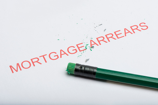 The word 'mortgage arrears' on paper with worn pencil eraser and eraser shavings, concept of growing debts or credit, financial problems