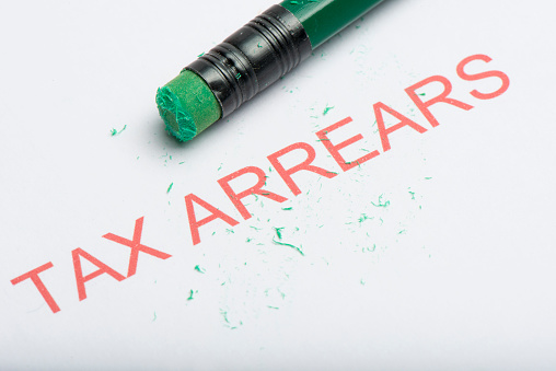 The word 'tax arrears' on paper with worn pencil eraser and eraser shavings, concept of growing debts or credit, financial problem