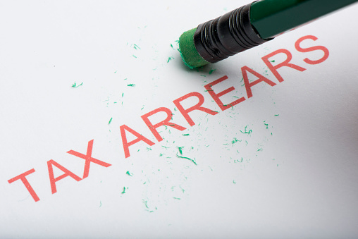 Pencil eraser trying to remove the word 'tax arrears' on paper, concept of growing debts or credit, financial problem