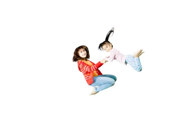 Picture of a beautiful woman playing with her daughter while jumping together in the studio