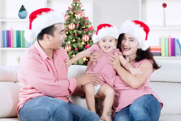 Picture of Asian family wearing Santa hat while laughing together and sitting on the couch