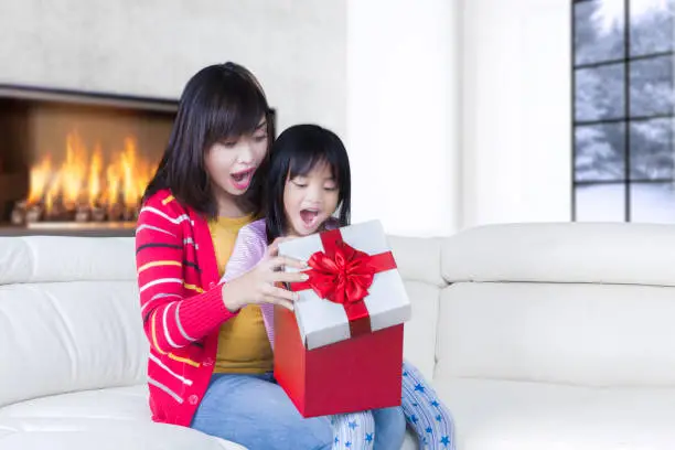 Portrait of young mother and cute child feeling surprised while opening a gift box together